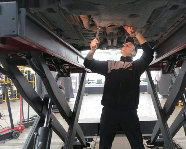 Automotive technician working underneath a lifted car in a workshop